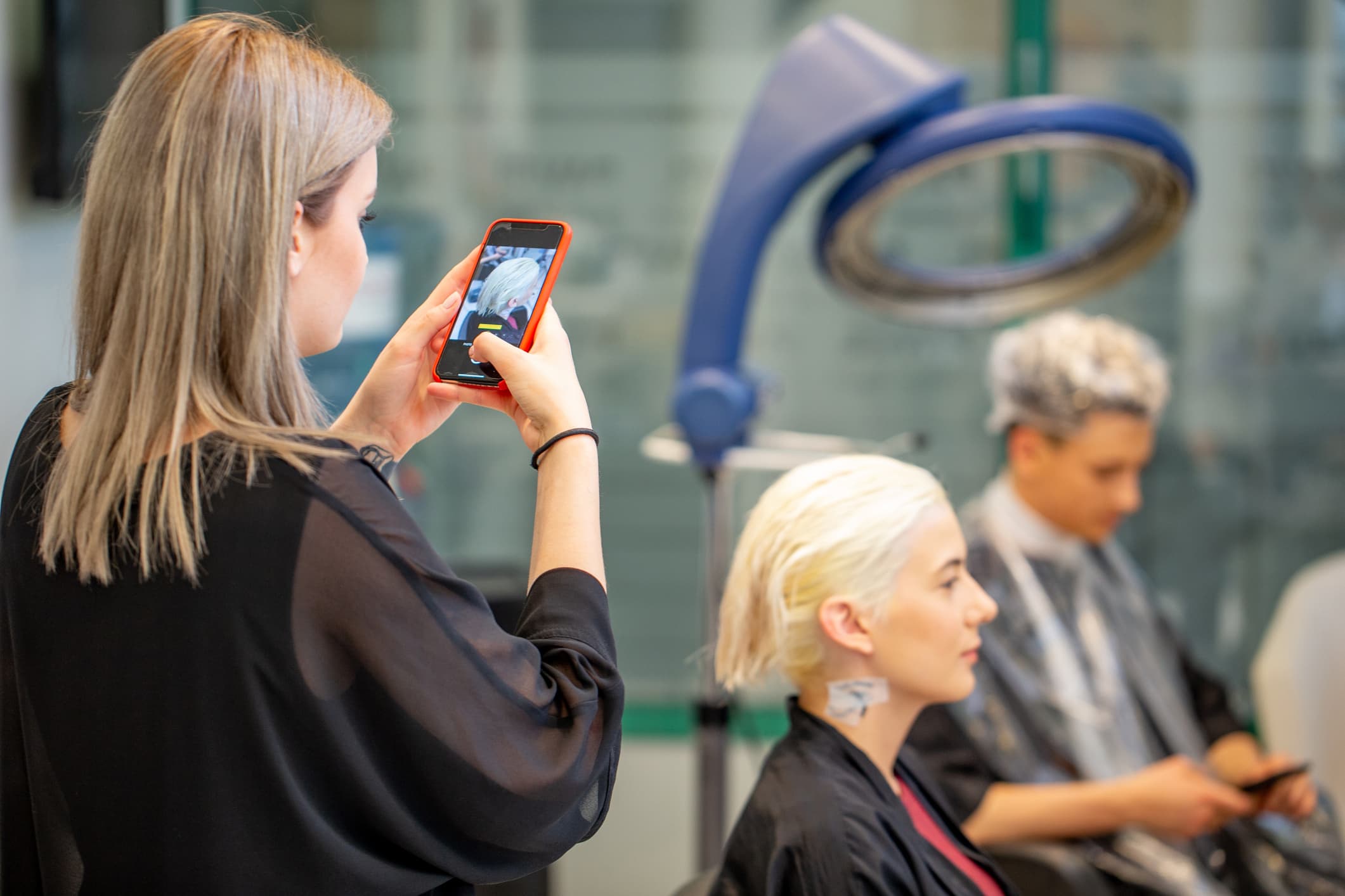 A stylist takes a picture of a client's haircut with her smartphone.