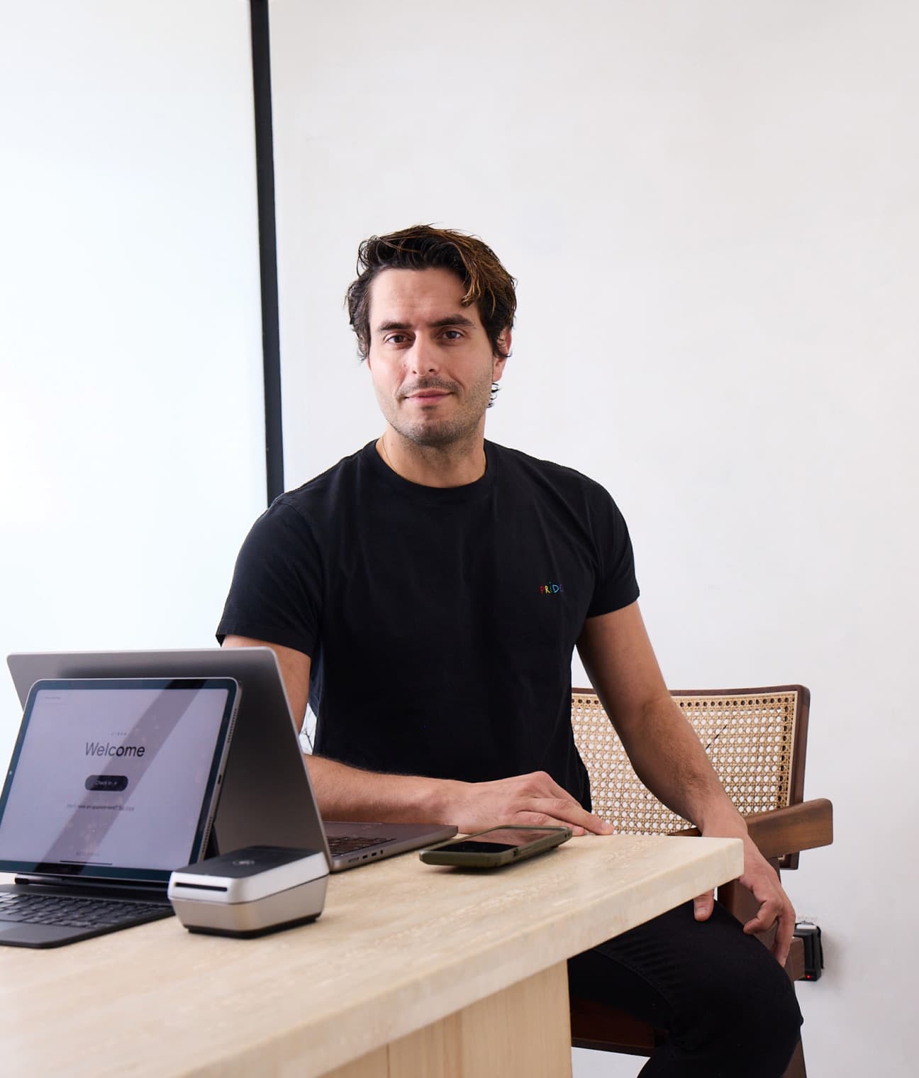 A barber leans on a front desk counter beside a laptop and the Boulevard Duo card reader showing a welcome screen.