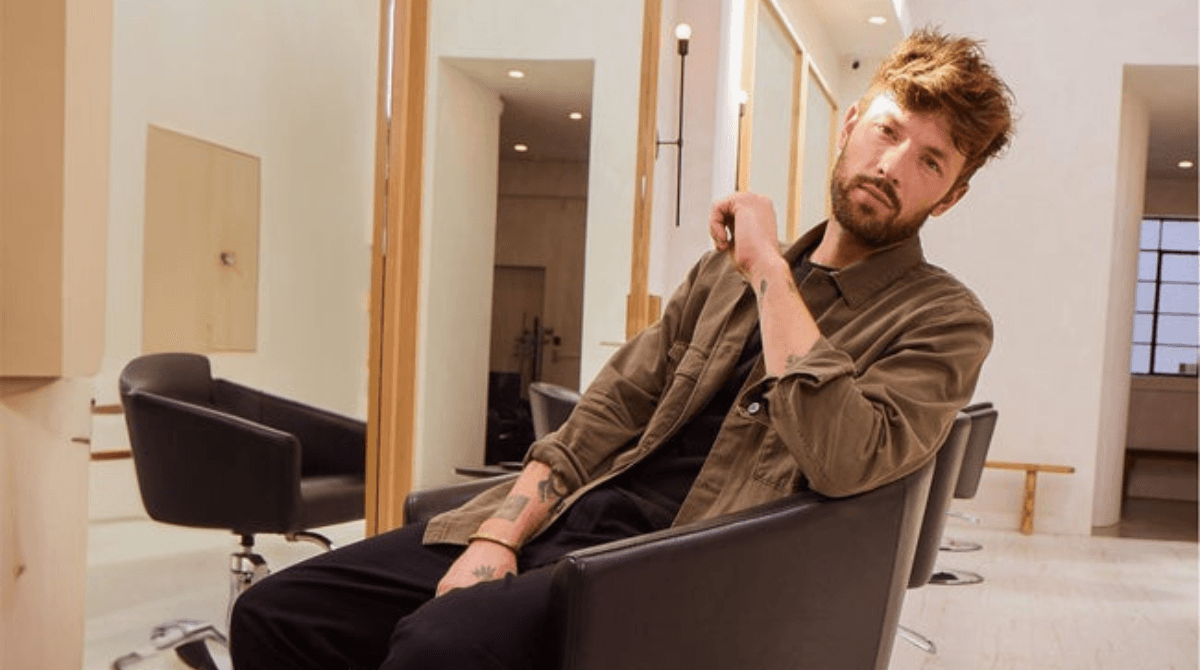 A stylist with impeccable hair sits casually in a chair at his salon.