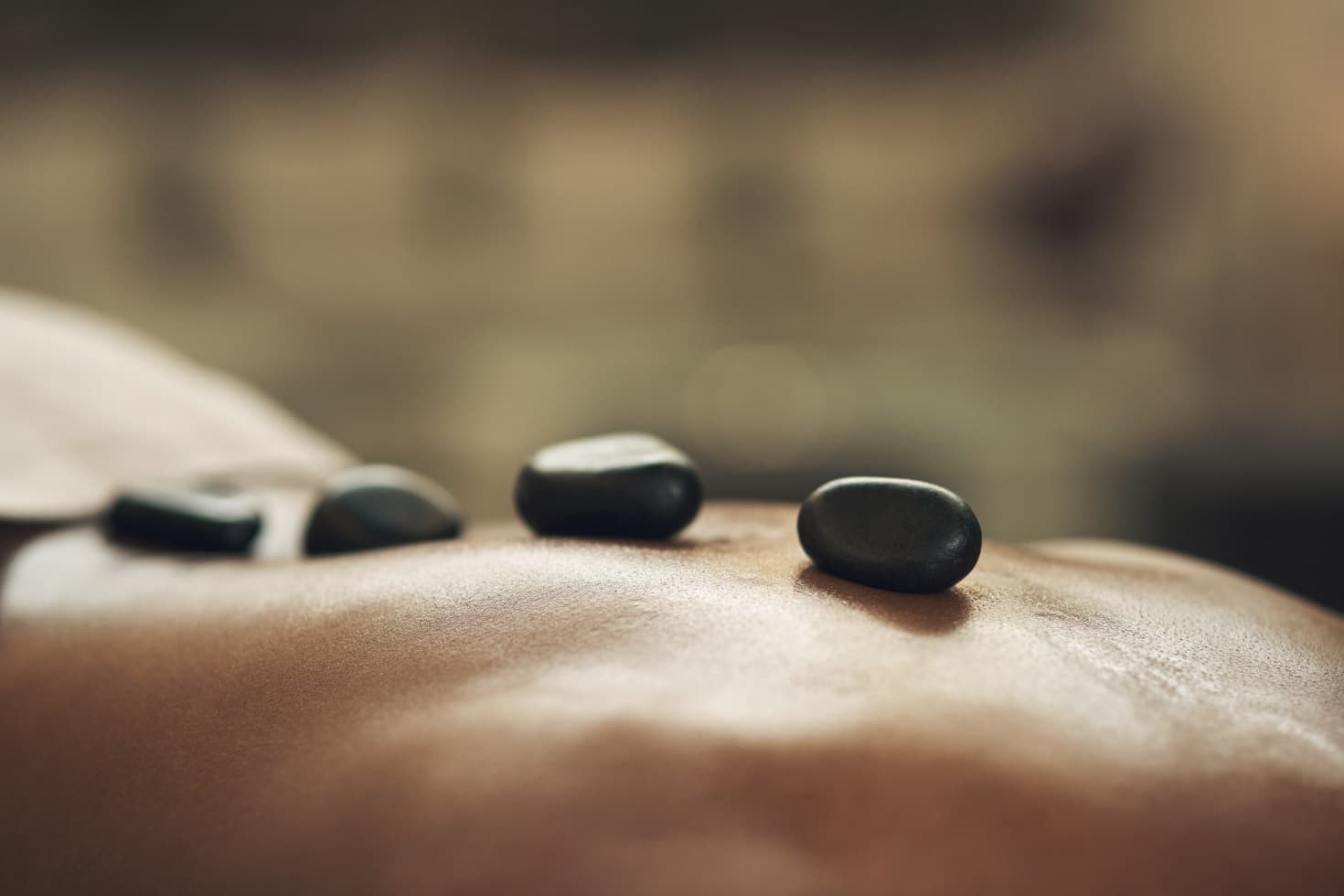 A row of shiny, tumbled black stones lay across a person's back.