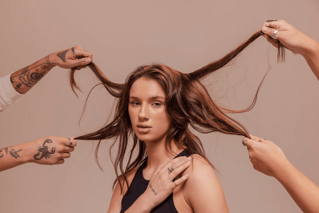 Several hands pull at the hair of one person standing in the center of the frame.